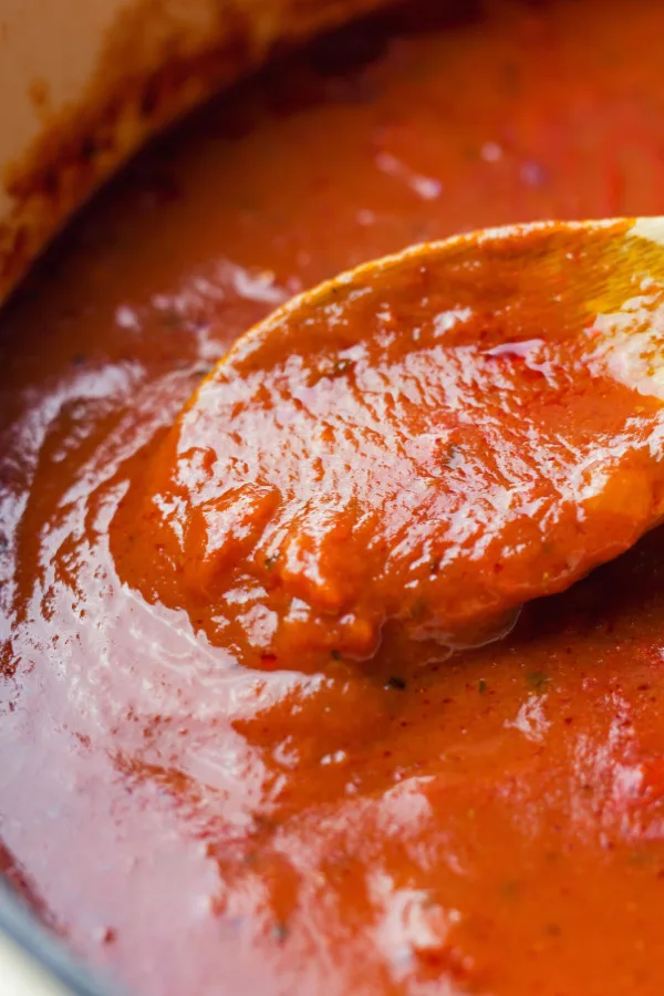 A thick batch of tomato sauce being stirred with a wooden spoon.